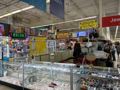 A bustling indoor market with colorful stalls, jewelry displays, and shoppers exploring various goods.